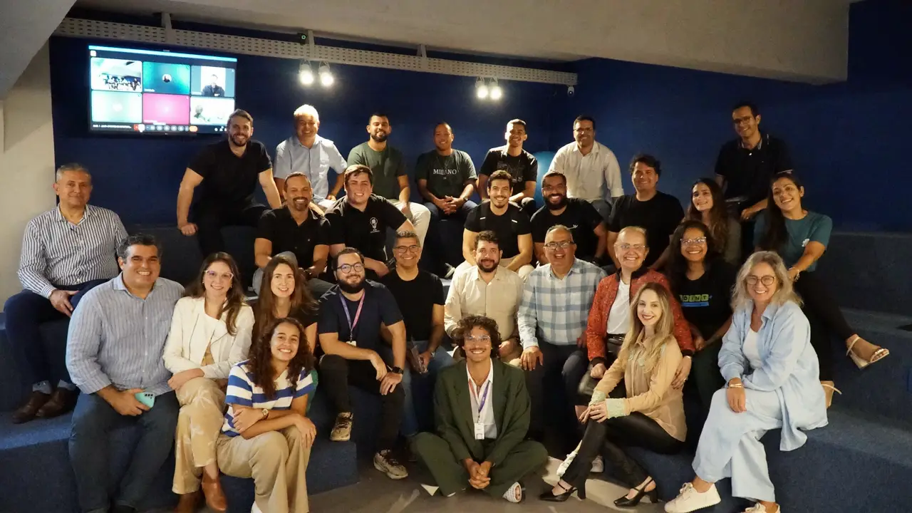 Cysneiros e equipe da 360 Consultoria posam com participantes da Joint sentados em arquibancada, com tela de videoconferência ao fundo.