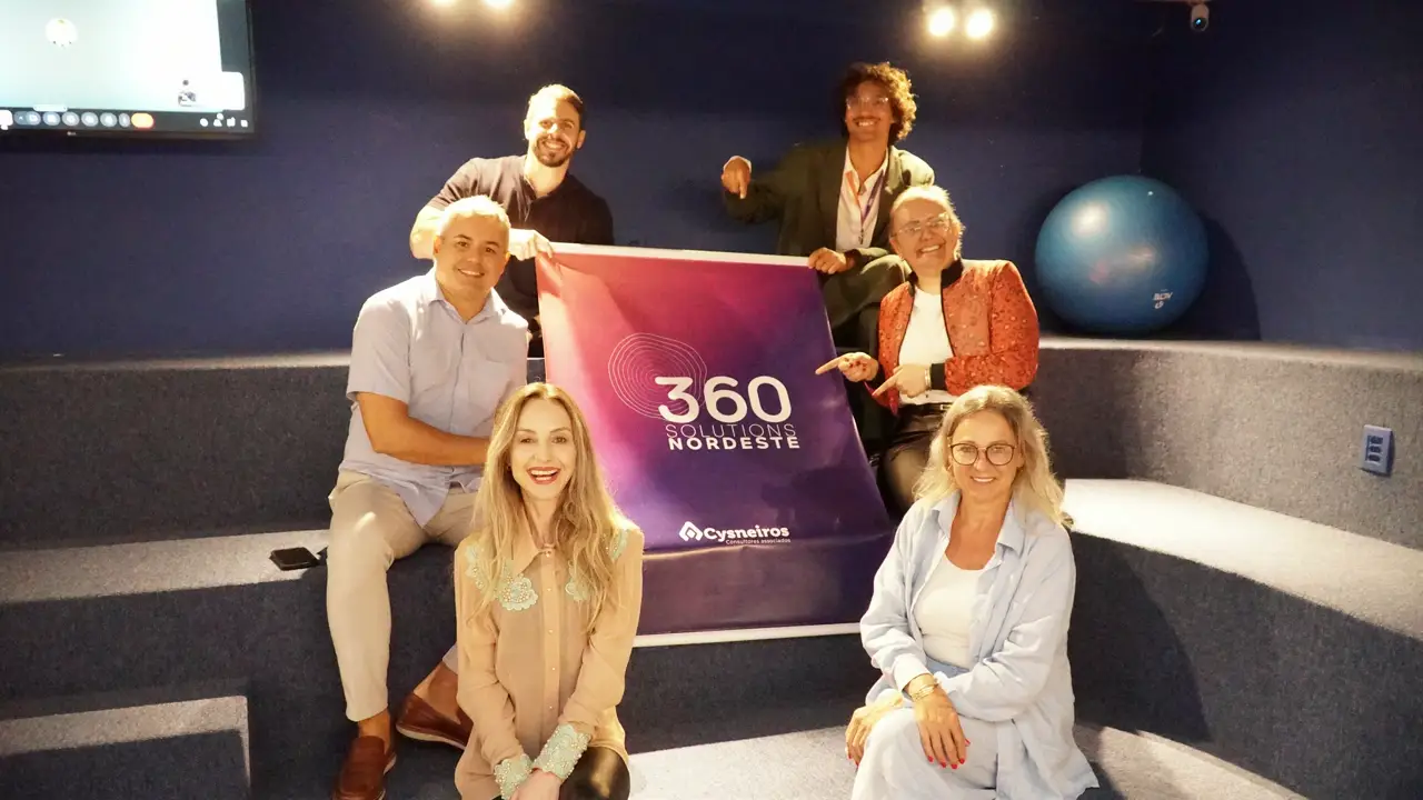 Cysneiros e equipe da 360 Consultoria posam com participantes do evento “Pontes de Oportunidade” em arquibancada interna.